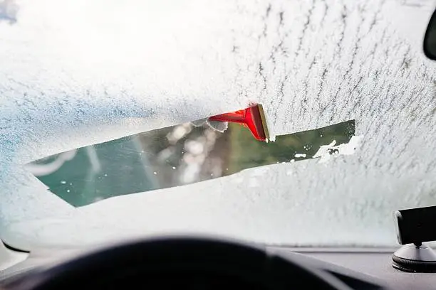 Photo of Woman deicing front car windshield with scraper