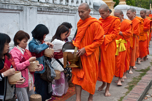 Luang Prabang, Laos - November 22, 2010: Barefoot Buddhist Monks collecting alms in the street from kneeling merit makers
