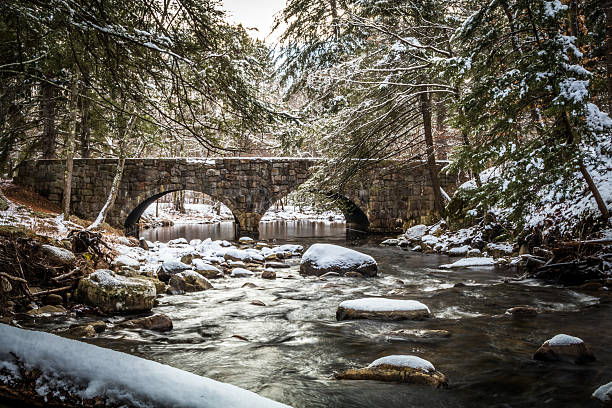 Tranquil winter river scene in the forest as snow covers rocks along the river and passes under a double arch stone bridge