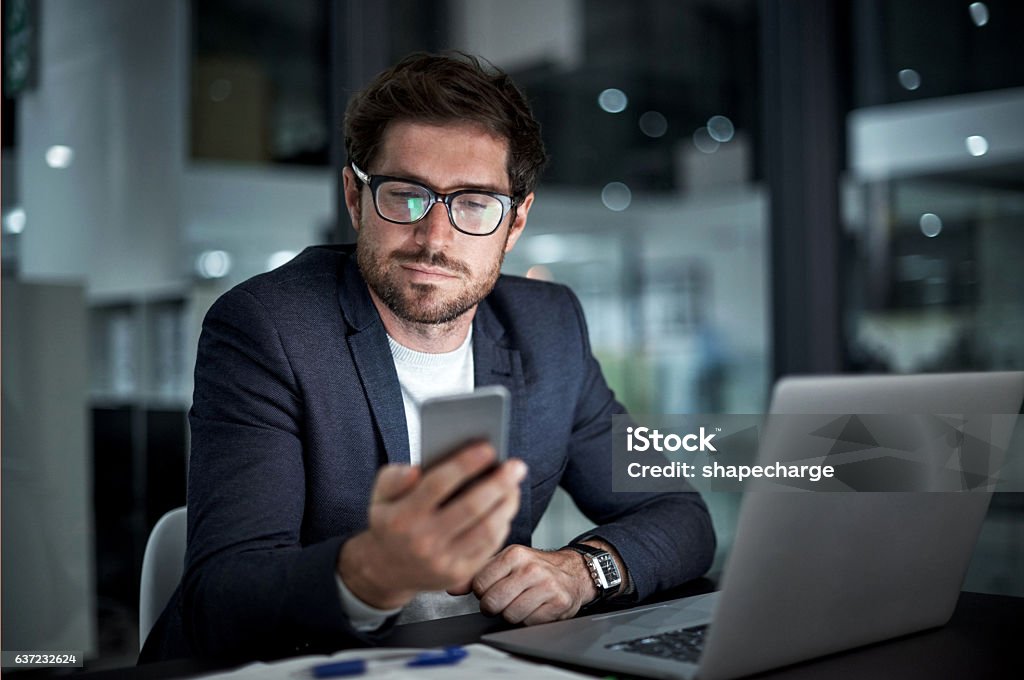 Enhancing his entrepreneurial ambition with the right tools Shot of a young businessman using his laptop and phone at work Mobile Phone Stock Photo