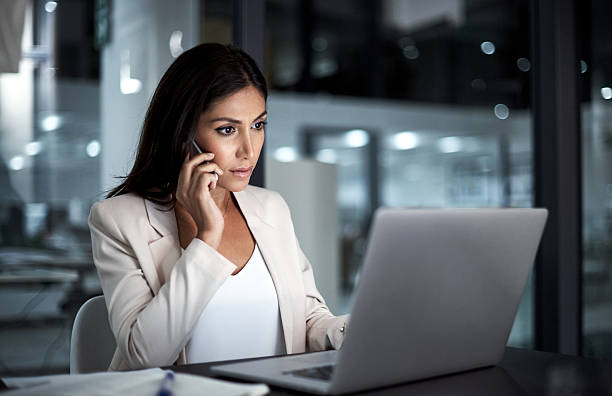 She’s the one to call to get it done Shot of a young businesswoman using her laptop and phone at work mobile phone finance business technology stock pictures, royalty-free photos & images