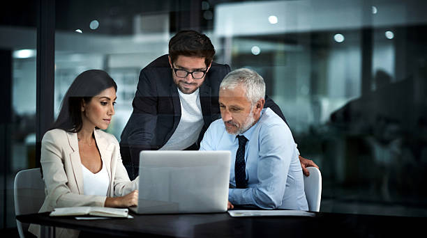 Three working as one successful unit Shot of colleagues using a laptop together at work serious business stock pictures, royalty-free photos & images