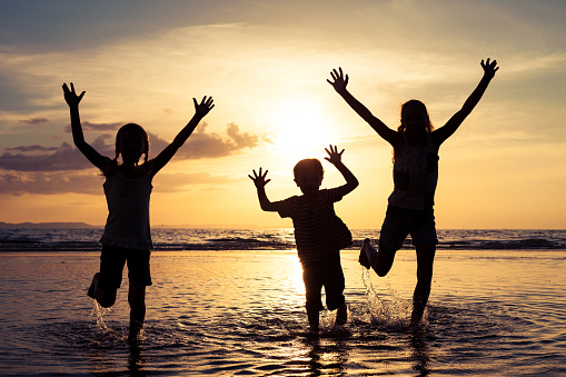 Happy children playing on the beach at the sunset time. Concept of happy friendly family.