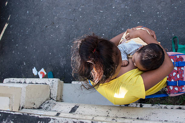 San Pablo City, Laguna, Philippines - May 16, 2005: Woman breast feeding a child selling candles at church yard.  A common scene found in many Third World Countries.