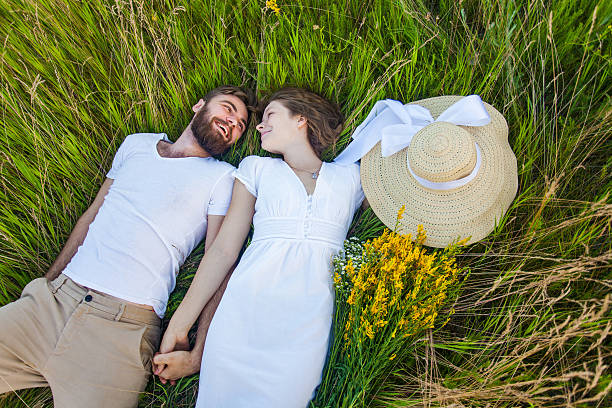 feliz joven pareja relajada en el amor acostado en la hierba. - cut flowers women field single flower fotografías e imágenes de stock