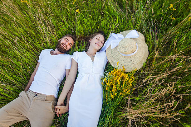 feliz joven pareja relajada en el amor acostado en la hierba. - cut flowers women field single flower fotografías e imágenes de stock