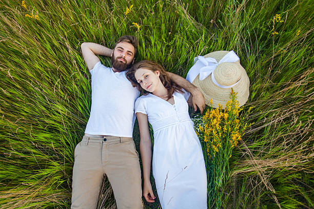 feliz joven pareja relajada en el amor acostado en la hierba. - cut flowers women field single flower fotografías e imágenes de stock