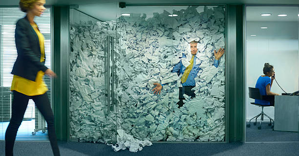 hold all calls A businessman is trapped in his glass office by a surplus of discarded ideas on paper . His colleague in the next office is working more efficiently and is oblivious to him being trapped , as is a passing female office worker careless stock pictures, royalty-free photos & images