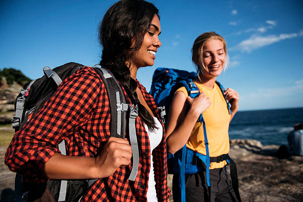 Two young woman taking a walk by the ocean carrying backpacks. Sydney, Australia.