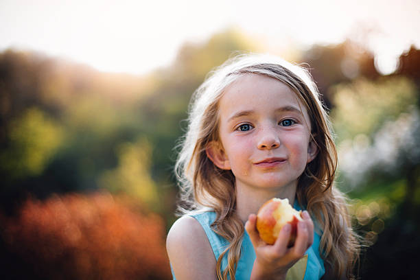 An Apple a Day Keeps the Doctor Away Little girl eating an apple. She is outdoors and looking at the camera, with apple juice on her face. one girl only stock pictures, royalty-free photos & images