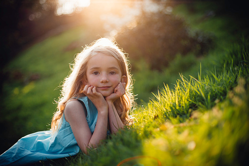 Beautiful little girl lying in the grass and posing for the camera. She has her head resting in her hands.