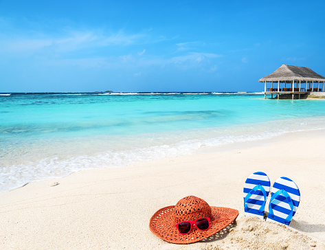 Sun hat with sunglasses and flip flops at tropical beach 