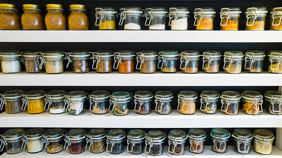Glass bottles with colorful spices on the white shelfs