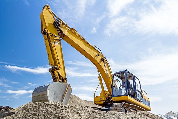 Excavator is preparing pile of sand for loading in truck. Yellow excavator is making pile of soil by pulling ground up on heap at construction site, project in progress. mechanical digger stock pictures, royalty-free photos & images