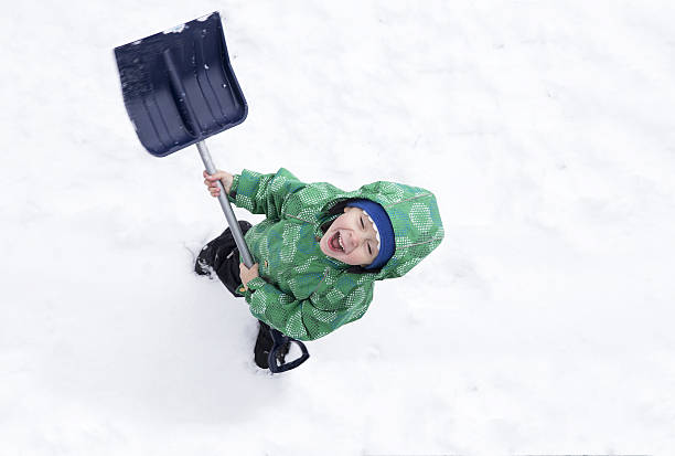 Portrait of a smiling girl, holding a snow shovel  in front of a snowy porch in a winter day.