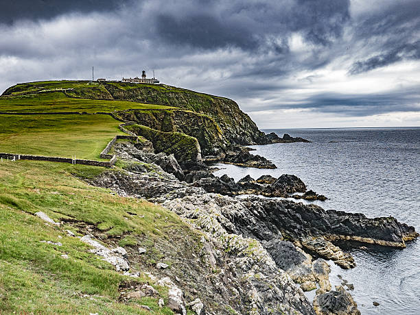 View of the Sumburgh Head Lighthouse on Mainland, Shetland, seen from the shoreline walking trail as moody storm clouds gather offshore.