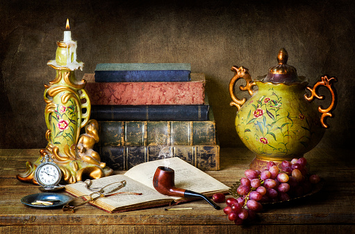 Classic still life with antiques,vintage books,old pipe, glasses,pocket watch and grapes on rustic wooden table.