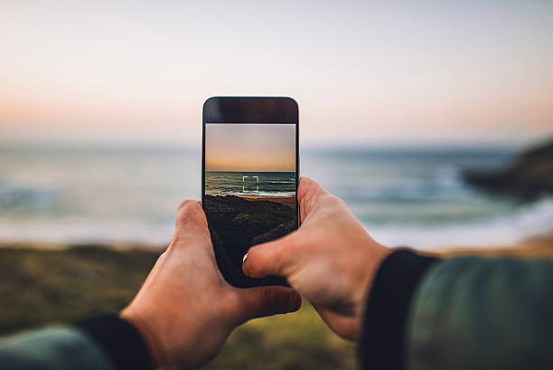 Two hands taking a picture with a mobile phone of a beach at sunset.