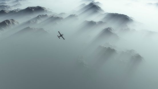 Aerial of single engine airplane over mountain range in thick layer of mist.