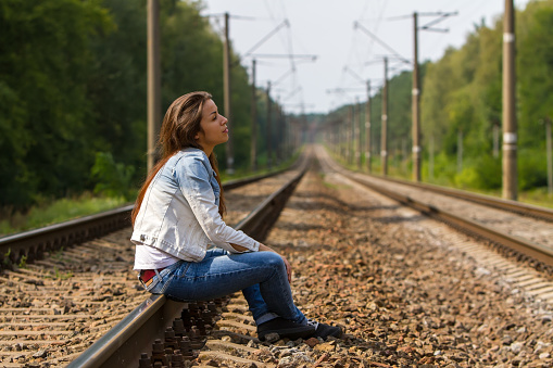The girl sits on rails and thoughtfully looks in the sky.