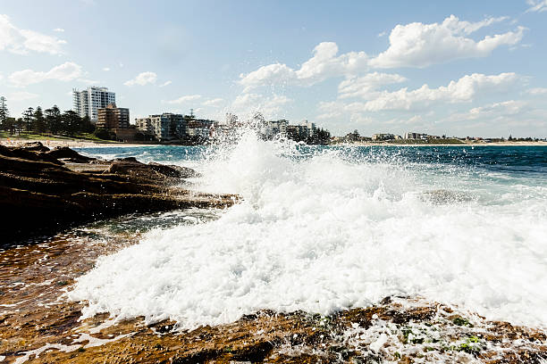 Beautiful water background with splashing ocean water over the rocks with bubbles and waves, coastline town in background, full frame horizontal composition with copy space