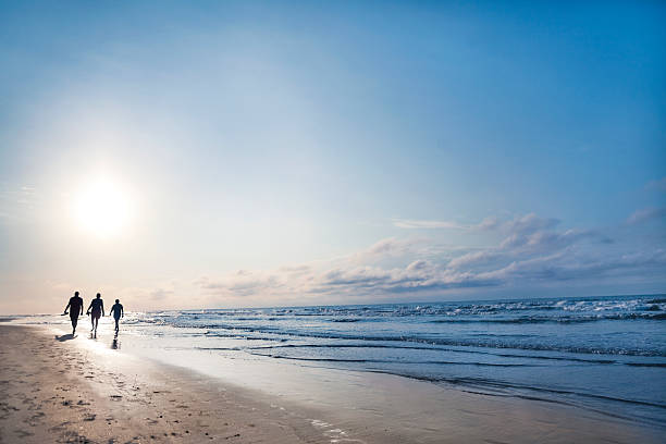 pessoas andando na praia ao nascer do sol - silhouette three people beach horizon - fotografias e filmes do acervo