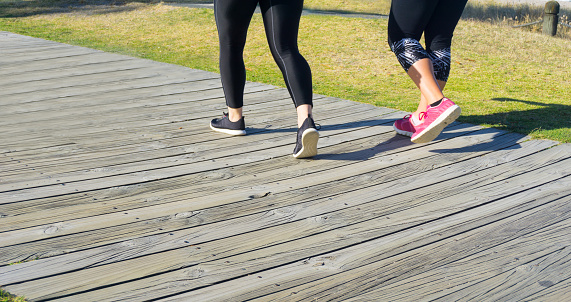 Two women's legs and shoes as they walk along a wooden boardwalk