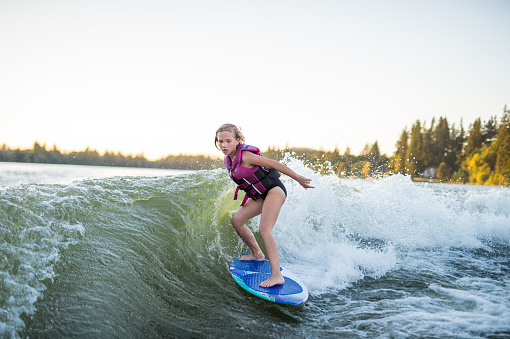 A young elementary aged girl is wakesurfing at sunset on a giant wake and is very focused