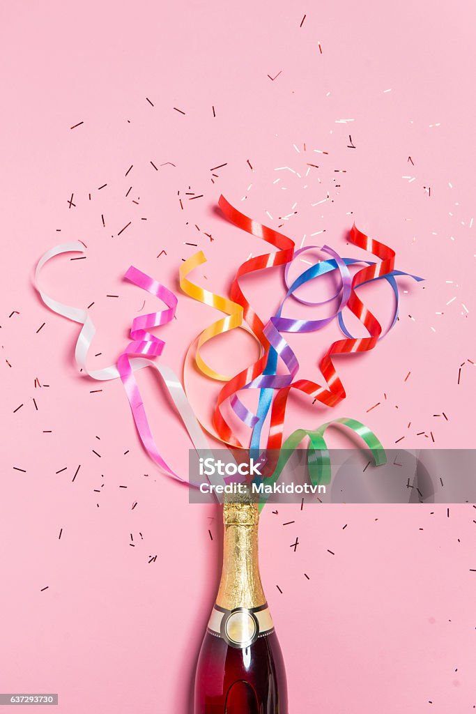 Champagne bottle with colorful party streamers on pink background. Flat lay of Celebration. Champagne bottle with colorful party streamers on pink background. Party - Social Event Stock Photo