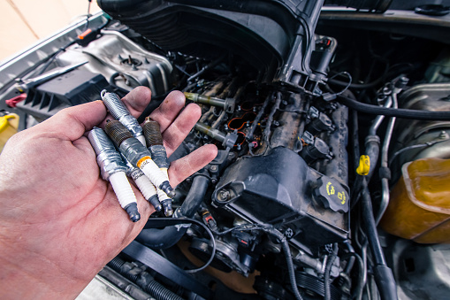 Holding old and new car spark plugs on engine