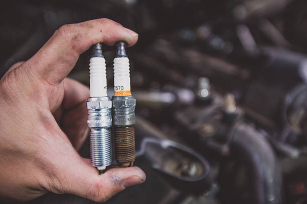 Holding old and new car spark plugs on engine stock photo