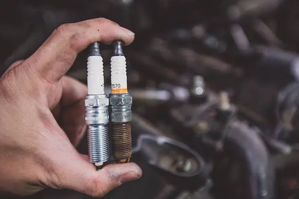 Photo of Holding old and new car spark plugs on engine