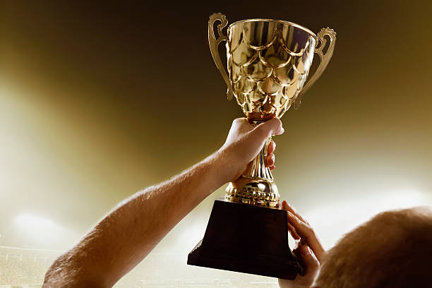 Athlete holding trophy cup above head in stadium Athlete holding trophy cup above head in stadium gold trophy stock pictures, royalty-free photos & images