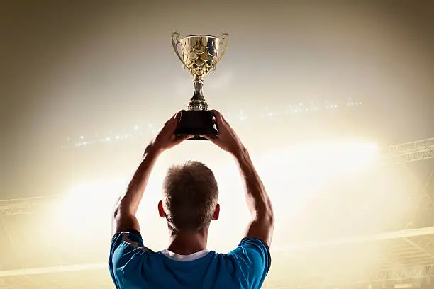 Photo of Athlete holding trophy cup above head in stadium