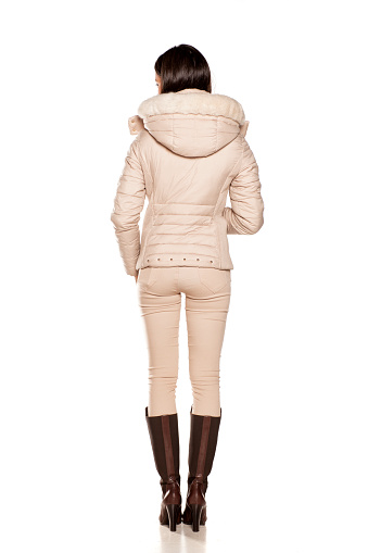 back view of a young woman in a winter jacket and boots posing on a white background