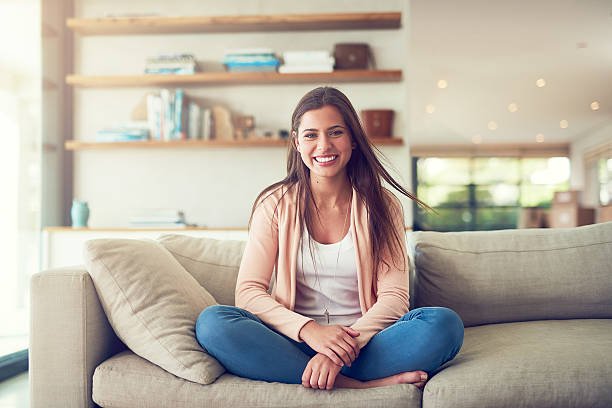 Enjoying a day to myself Portrait of a smiling young woman relaxing on the sofa at home cross legged stock pictures, royalty-free photos & images