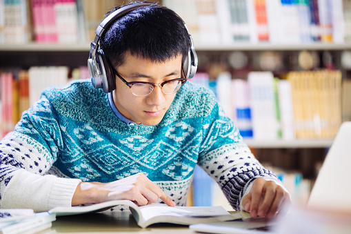 young asian man student studying with headset in library