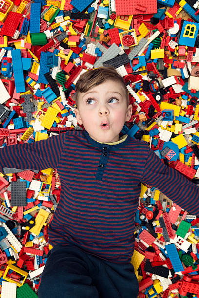 playful boy between plastic blocks A little happy blond boy with blond hair and blue eyes lies between a lot of colorful plastic blocks toy / building blocks. little boys blue eyes blond hair one person stock pictures, royalty-free photos & images