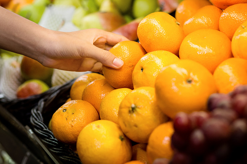 woman's hand choosing orange in supermarket