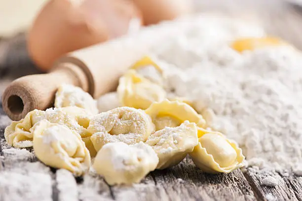 Homemade raw Italian tortellini on wooden vintage cutting board with a rolling pin