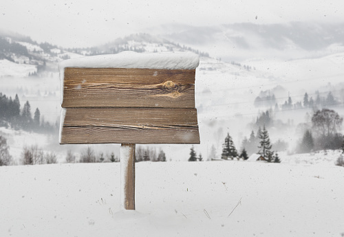 Wooden signpost with less snow on it and snowfall and mountains on background