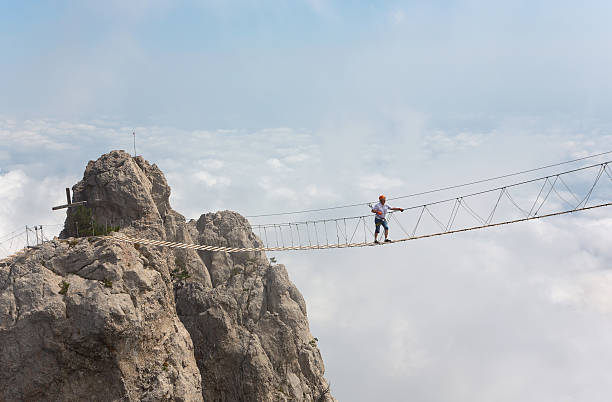 Man crossing the chasm Man crossing the chasm on the hanging bridge (focus on the man) ravine photos stock pictures, royalty-free photos & images