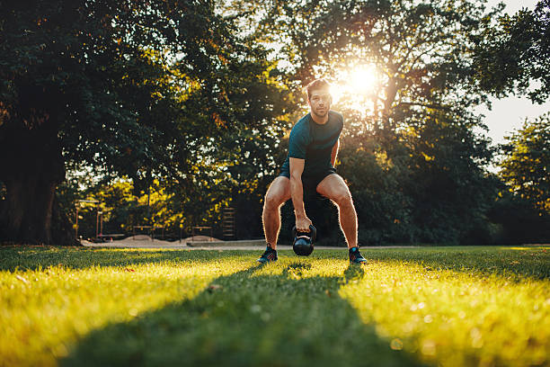 fitness young man training with kettlebell in the park - sportsman looking at camera full length sport imagens e fotografias de stock