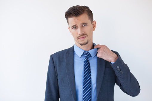 Closeup of tired middle-aged business man pulling his collar, feeling hot and looking at camera. Isolated view on white background.