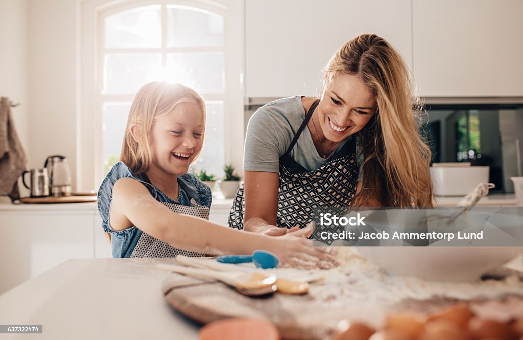 Happy young girl with her mother making dough Happy young girl with her mother making dough. Mother and daughter baking in kitchen. Cooking Stock Photo