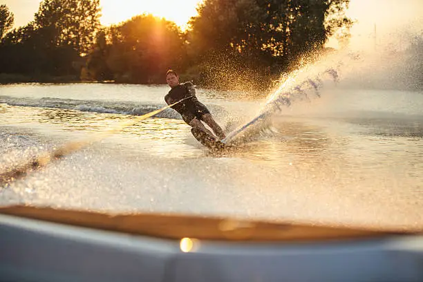 Man wakeboarding on lake behind boat. Water skiing on lake at sunset.