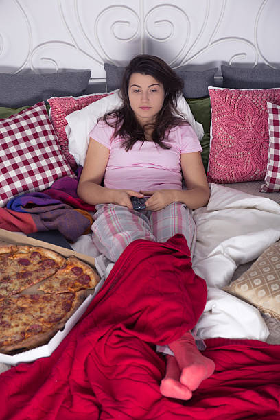 Single woman eating pizza Single woman lying in bed, eating pizza and watching tv divorcee stock pictures, royalty-free photos & images