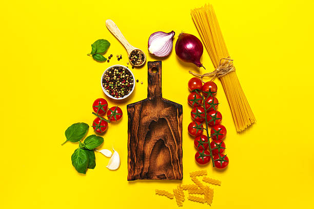 Italian food or ingredients background with fresh vegetables, pasta, cheese parmesan and spices. Top view, view from above. Vibrant yellow background