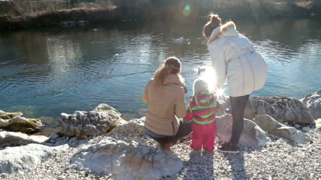 Beautiful river scene with two mothers and a baby feeding birds