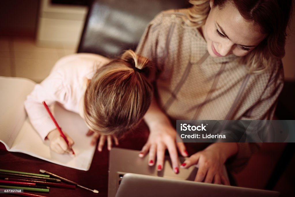 Busy mom. Above view of mother using laptop and her little daughter drawing at home. Mother Stock Photo